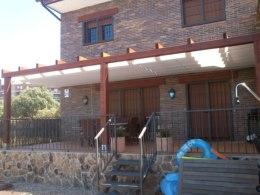 Pergola de madera independiente, en color nogal con toldos corredizos.